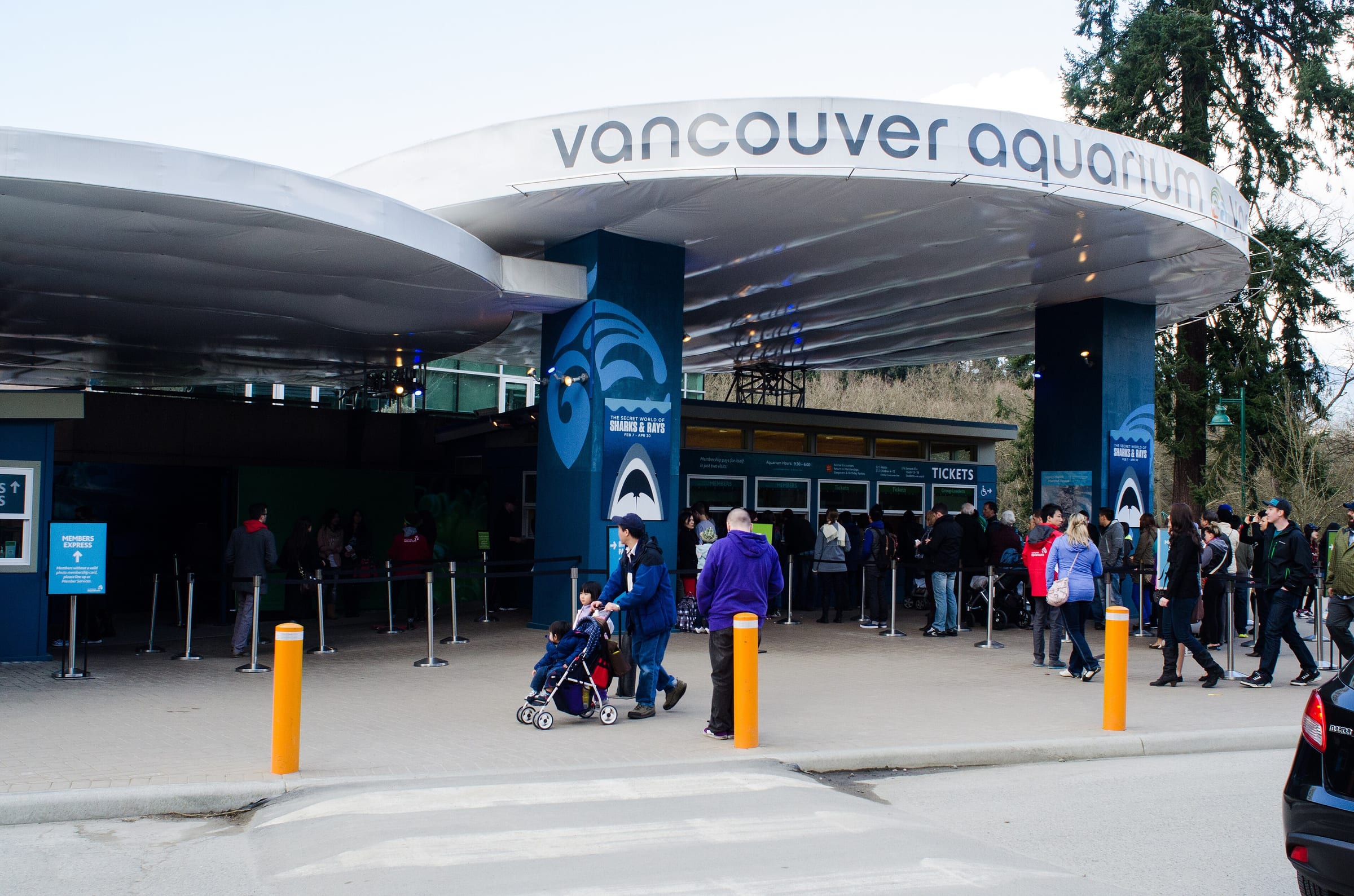 Visitors queue under the curved canopy at the entrance of the Vancouver Aquarium in Stanley Park.